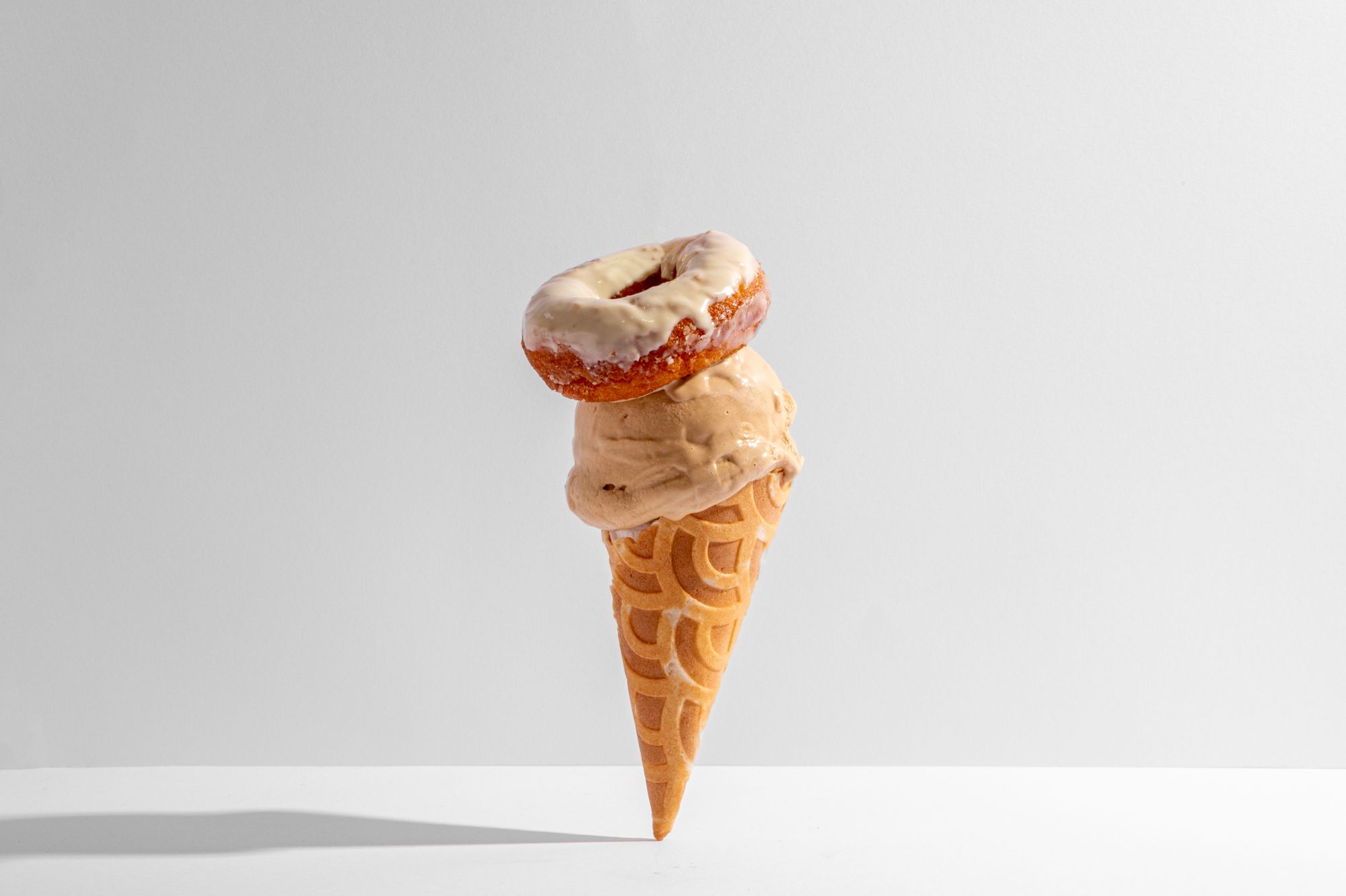 An ice cream cone with a donut sitting on top of the pile of ice cream.