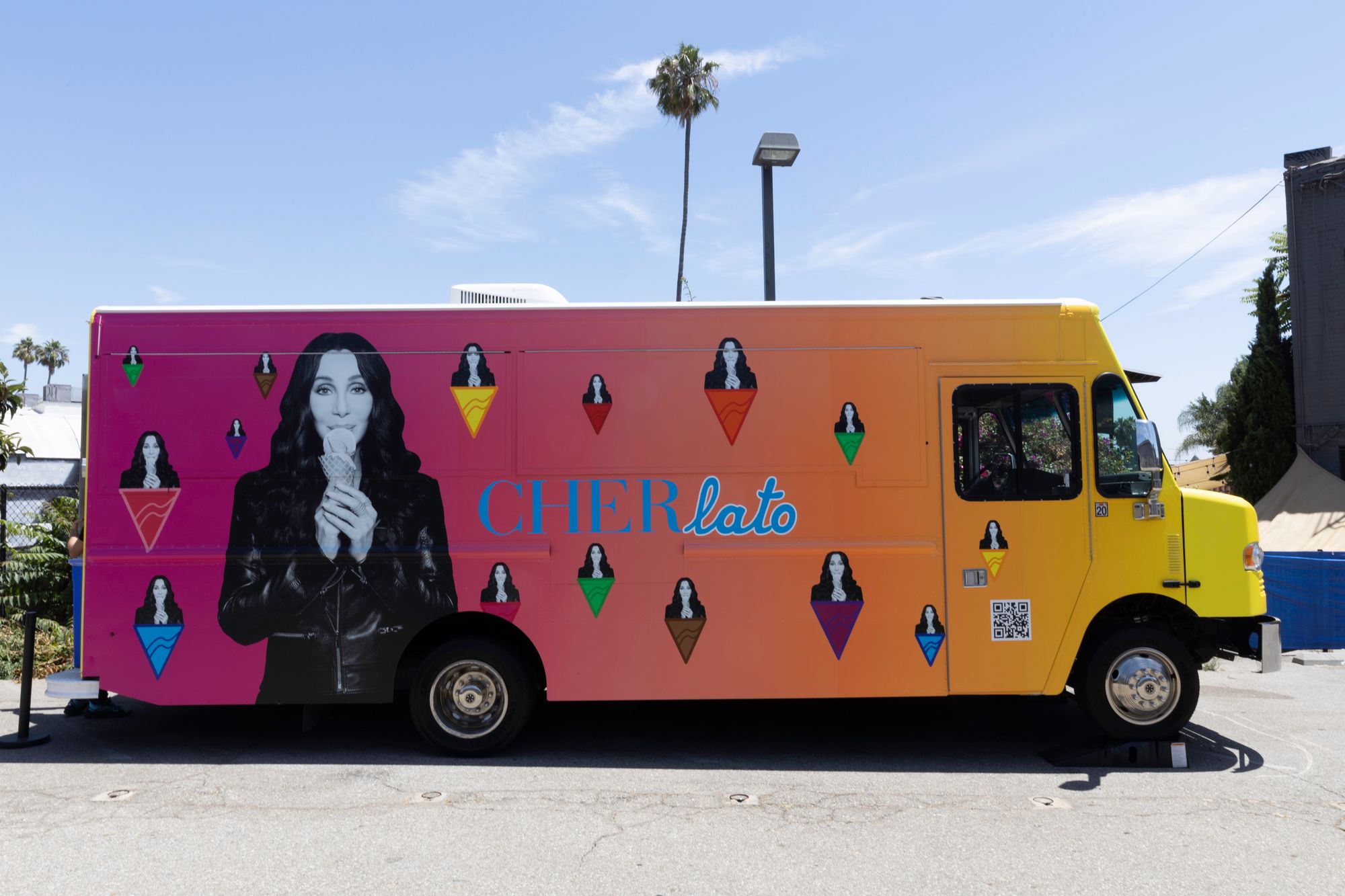 A multi-colored ice cream truck with multiple images of Cher on the side. The word "Cherlato" is written on the side of the truck.