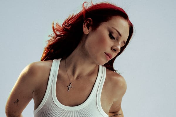 Rose Gray: A white woman with red hairs wears a white tank top and a cross around her neck.