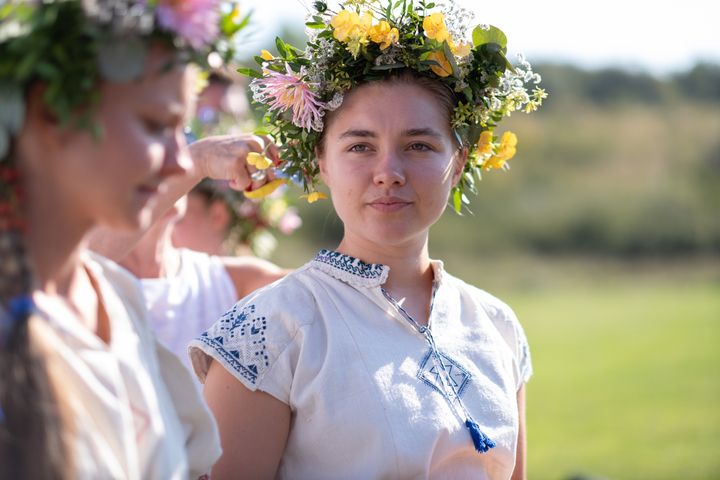 Actress Florence Pugh has a white linen shirt on and she wears a flower crown.